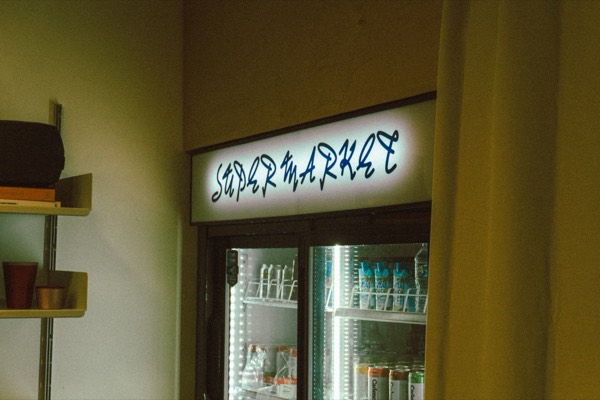 The lit Supermarket sign above a drinks fridge