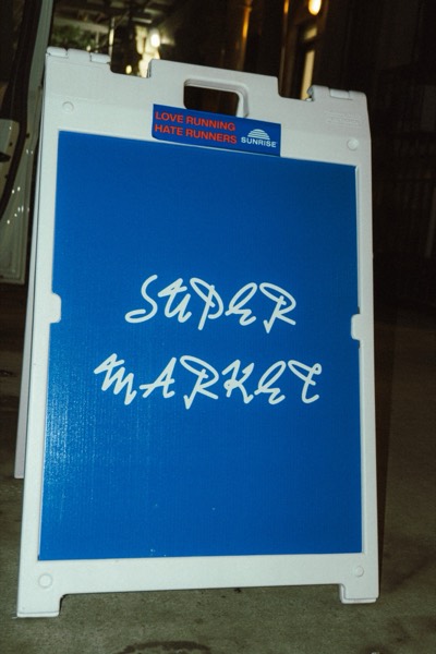 The blue Supermarket sandwich-board sign on the sidewalk at night