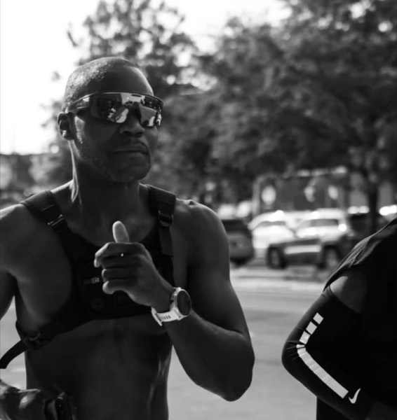 A runner in mirrored sunglasses giving a thumbs up, in black and white, at WEPA 9 for 9